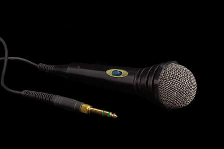 Dynamic microphone in black plastic housing with windscreen in wire mesh  and its phone connector on a dark backgroundの写真素材