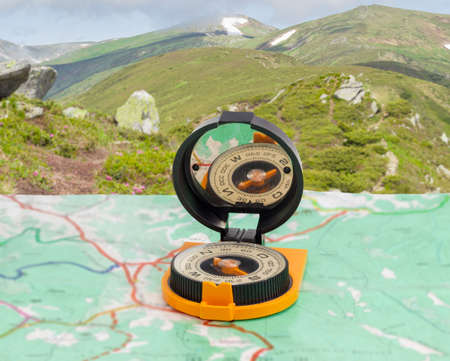 Magnetic compass with mirror of sighting mechanisms on a tourist topographical map against the background of a mountain rangeの写真素材