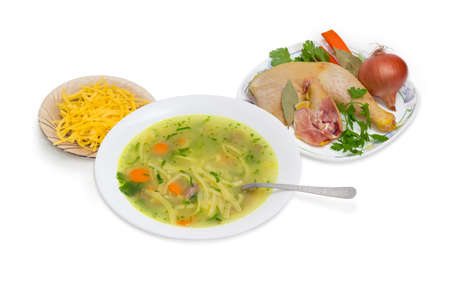 Homemade chicken noodle soup in white dish with spoon and ingredients for its cooking on a light backgroundの写真素材