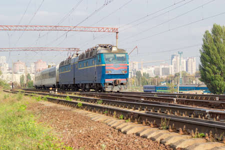 Passenger inter-city train with electric locomotive on the background of urban development in autumn dayの写真素材