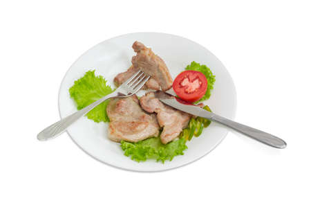 Three slices of fried pork neck on lettuce leaves, slices of tomato and green chili, fork and knife on white dish on a light backgroundの写真素材