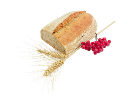 Partially cut wheat sourdough bread, sprinkled with sesame seeds, two spikes of ripe wheat, cluster of red rowan on a light backgroundの写真素材