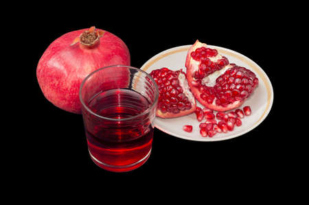 Pomegranate juice in a glass, one whole pomegranate and peeled pomegranate on a saucer on a dark backgroundの写真素材