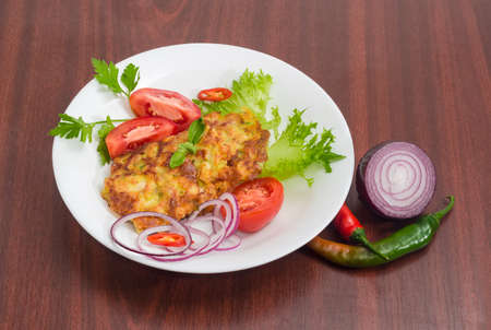 Chopped cutlets made of pork with lettuce and tomatoes decorated with chili and red onion slices and twigs of parsley and basil on white dish on a dark wooden surfaceの写真素材