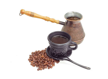 Old copper coffee pot with freshly brewed coffee, coffee in black ceramic cup with saucer and spoon and pile of roasted coffee beans on a light backgroundの写真素材
