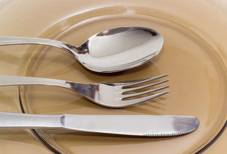 Eating utensils consisting of spoon, fork and knife made from stainless steel on a dark glass dish...
