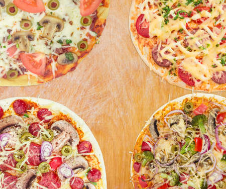 Fragments of four different cooked round pizza on a light wooden surfaceの写真素材