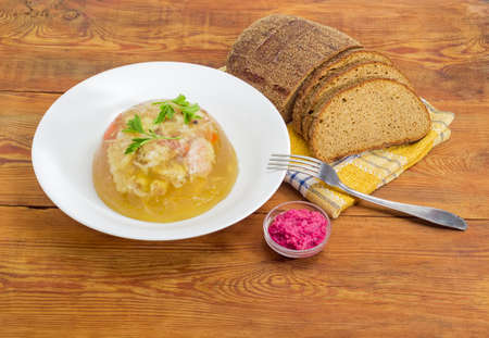 Pork aspic in white dish, brown bread, fork, beet horseradish sauce in small glass container on a surface of a old wooden planks の写真素材