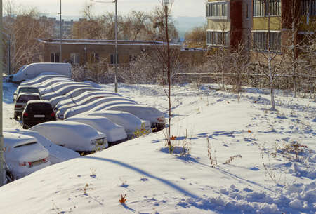 Cars, covered with fluffy snow on the parking lot in a residential area at a sunny morningの写真素材
