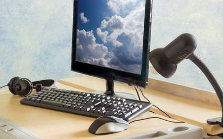 Workplace with monitor, keyboard, mouse, headphones and light fixture on a working student table
の写真素材