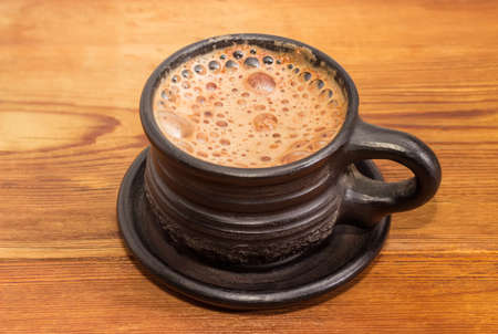Freshly brewed coffee latte in a black ceramic cup on an old wooden surface closeup