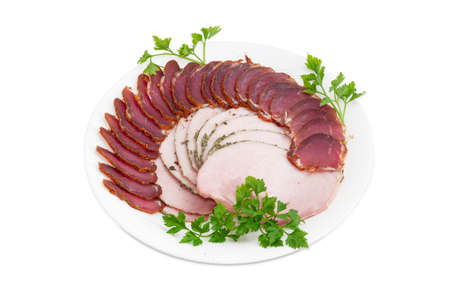 Sliced dried pork tenderloin and ham with twigs of parsley on a white dish on a light backgroundの写真素材