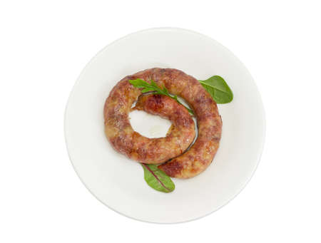 Top view of freshly roasted pork sausage in natural casing with few leaves of different leafy greens on a white dish on a light backgroundの写真素材