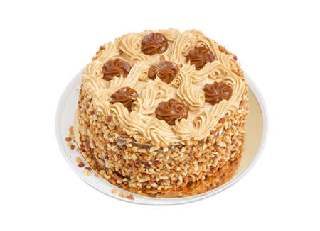 Round sponge cake, decorated with butter cream and caramelized condensed milk, sprinkled with grated nuts on a light backgroundの写真素材