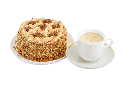 Round sponge cake, decorated with butter cream and caramelized condensed milk, sprinkled with grated nuts and coffee with cream in white cup on a light backgroundの写真素材