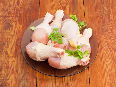 Uncooked chicken legs and twigs of parsley on a glass dish on an old wooden surface
の写真素材