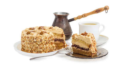 Partly sliced layered sponge cake, decorated with butter cream, caramelized condensed milk and nuts on background of coffee cup and old coffee pot on a light backgroundの写真素材