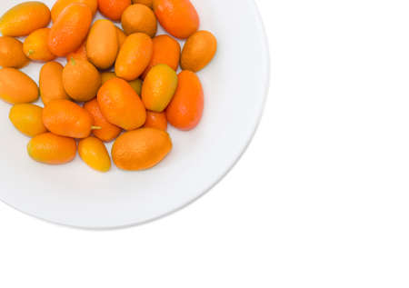 Top view of fragment of white dish with fresh oval kumquats closeup on a light backgroundの写真素材