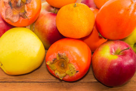 Pile of ripe fresh persimmons, apples and mandarin oranges on an old wooden surface closeupの写真素材