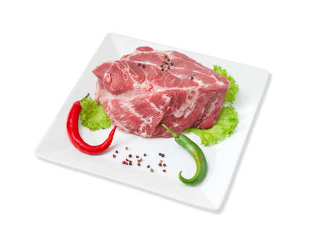 Piece of a fresh uncooked pork neck, green and red chili, black and red pepper, lettuce on a white square dish on a light backgroundの写真素材