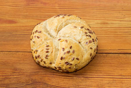 Round wheat sourdough bun, sprinkled with flax and sesame seeds on an old wooden surfaceの写真素材