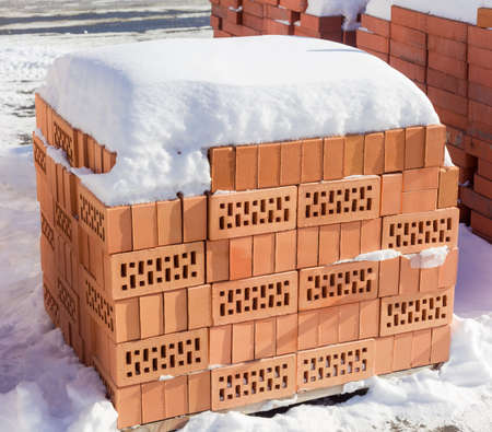 Red perforated bricks with rectangular holes covered snow on a pallet on an outdoor warehouse in...
