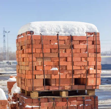 Wooden pallet of the red bricks covered snow on an another such pallet on a outdoor warehouse in winter sunny dayの写真素材