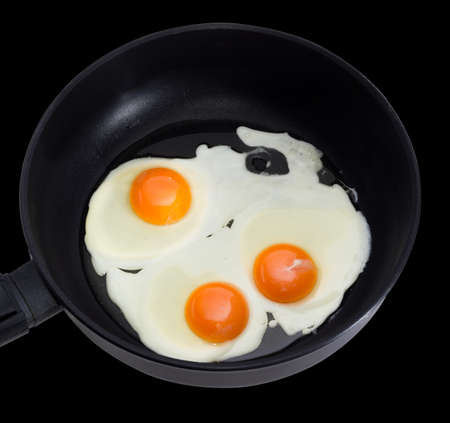 Three fried eggs prepared by sunny side up on the frying pan during cooking closeup on a dark...