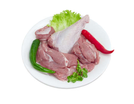 Uncooked turkey meat with the lettuce, parsley and the green and red chili on a white dish on a light backgroundの写真素材