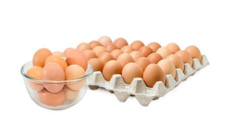 Glass bowl with the brown chicken eggs against the background of the cardboard egg tray of eggs on a light backgroundの写真素材