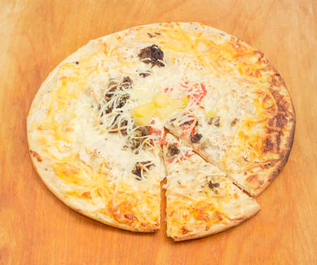 Cooked and partly sliced round pizza with mushrooms, tomatoes and plenty of cheese on a wooden cutting boardの写真素材