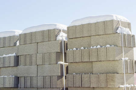 Concrete masonry units packed on pallets and covered snow closeup on an outdoor warehouse in winter sunny dayの写真素材