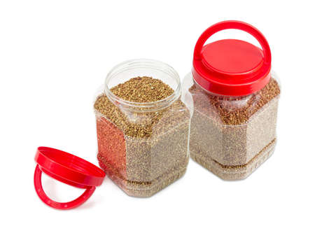 Buckwheat groats peeled from the husk in two transparent plastic containers with the red covers, one of them open on a light backgroundの写真素材