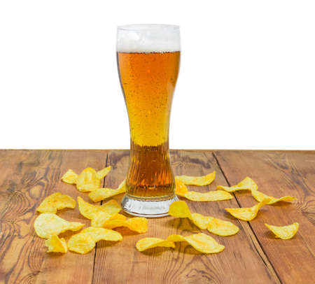 Beer glassware with the lager beer among the potato chips scattered the old wooden planks on a light backgroundの写真素材