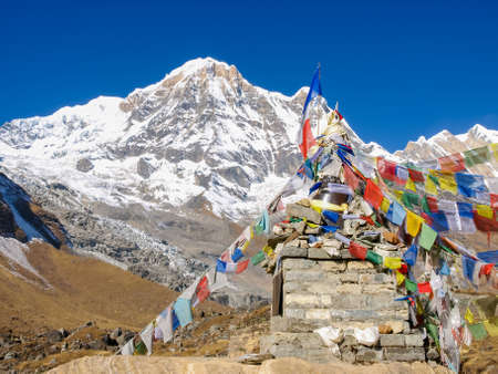 Small stupa and colorful prayer flags on the background of the Annapurna South Mountain and a sky in morning in the Himalayasの写真素材