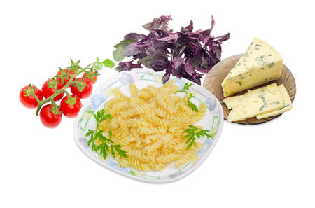 Cooked spiral pasta and the parsley twigs on a dish, cluster of the red cherry tomatoes, blue cheese on a glass saucer and bundle of the purple basil on a light backgroundの写真素材
