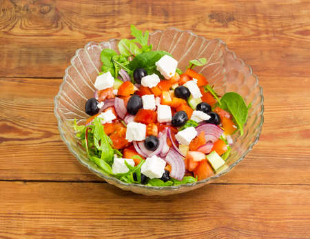 Greek salad in the glass salad bowl on a surface of an old wooden planksの写真素材