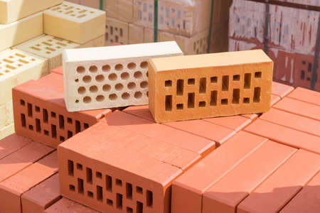 White brick with a round holes and yellow brick with a rectangular holes from above on a pallet with the red perforated bricks on the background of other bricks on a warehouseの写真素材