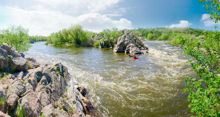 Panorama of the river section with rapids and kayaks, rock outcrops and trees on its banks on a spring day
の写真素材