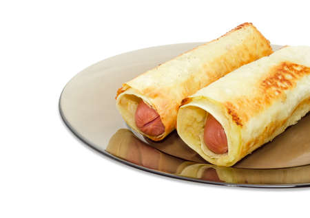 Fragment of the dark glass dish with two baked sausage rolls made of the Vienna sausages and mashed potatoes wrapped in puff pastry closeup on a light backgroundの写真素材