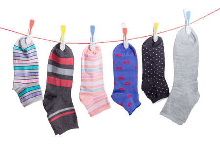 Several different varicolored men's and women's socks hanging on the clothes line with plastic clothespins on a light backgroundの写真素材