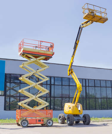Wheeled scissor lift and wheeled articulated lift with telescoping boom and basket on an asphalt...