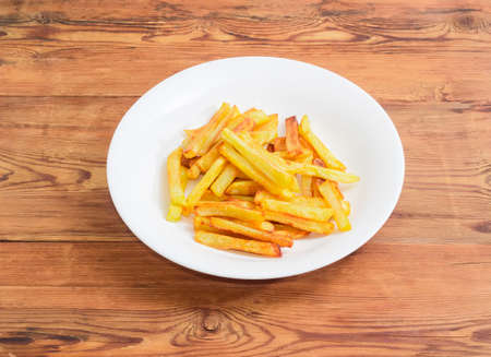 French fries on the white dish on a surface of old wooden planks