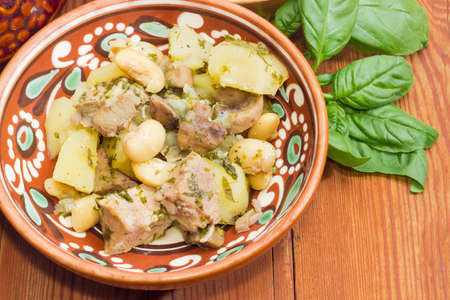 Ukrainian version of the dish Chanakhi in a clay bowl  - potatoes with meat, mushrooms and haricot beans on a surface of an old wooden planks closeupの写真素材