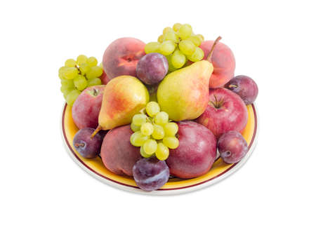 Several apples, pears, plums, peaches and clusters of white grapes on the big yellow dish on a white backgroundの写真素材