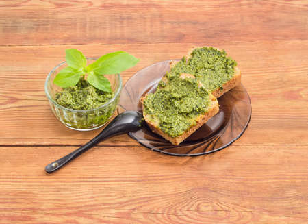 Two sandwiches with pesto on glass saucer and small black spoon, sauce pesto in small glass bowl...