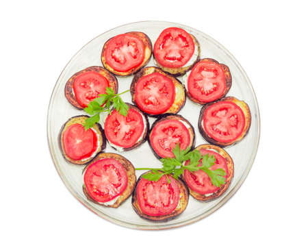 Top view of a glass dish with chopped by circles roasted eggplants with garlic sauce and covered by chopped fresh tomatoes on a white backgroundの写真素材