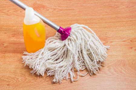 Classic mop with cotton head and metal tubular handle and plastic bottle of floor cleaner on a...