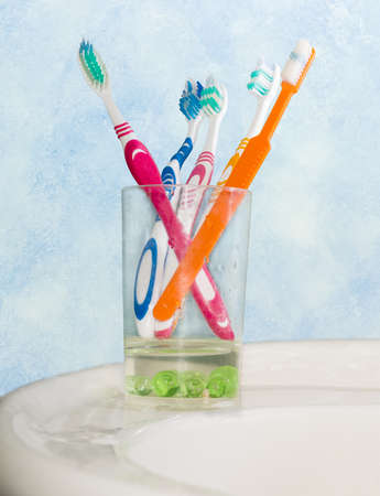 Several different toothbrushes in glass for toothbrushes on handbasin on a background of blue wall の写真素材