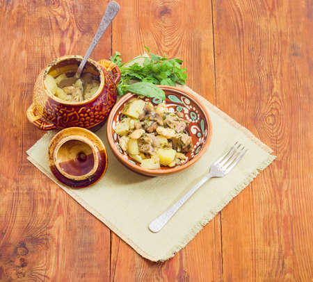 Ukrainian version of the dish Chanakhi in a clay bowl on a napkin - potatoes with meat, mushrooms and haricot beans baked in a clay pot on a surface of an old wooden planksの写真素材